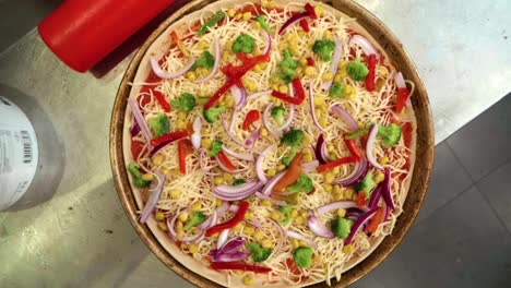 Bird's-eye-view-slow-motion-shot-of-pizza-with-onions,-cheese,-peppers,-broccoli,-and-tomato-sauce,-camera-moving-up