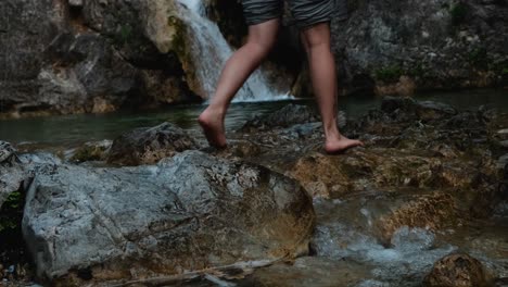 young woman crosses a stream barefoot with beautiful waterfall in mount olympus, greece