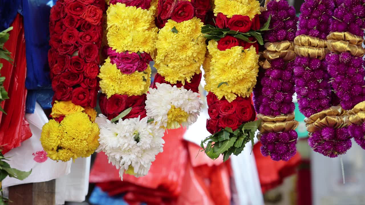 Vibrant flower garlands hang in rows at an outdoor market stall in Singapore’s Little India, captured with shallow depth of field and gentle camera pan