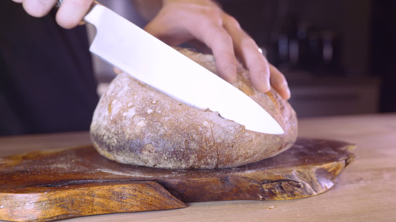Uomo che affetta pane di pasta madre fresco fatto in casa in cucina - primo piano, ripresa con slider a sinistra