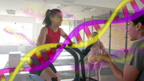 Animation-Eines-DNA-Strangs-über-Einer-Kaukasischen-Trainerin-Und-Einer-Frau-Beim-Crosstraining-Auf-Dem-Crosstrainer-Im-Fitnessstudio