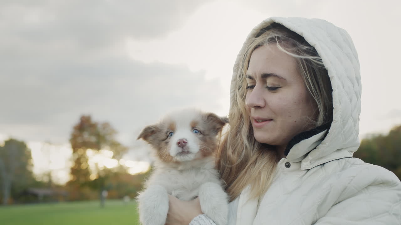 A young woman holds a cute puppy in her hands, a puppy licks her face. Walking together in an autumn park.