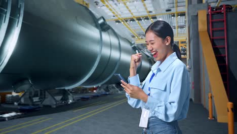 side view of happy asian business woman celebrating using mobile phone in pipe manufacturing factory