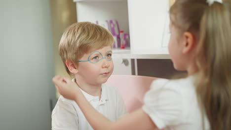 la niña pinta la cara del hermano menor con lápiz de color