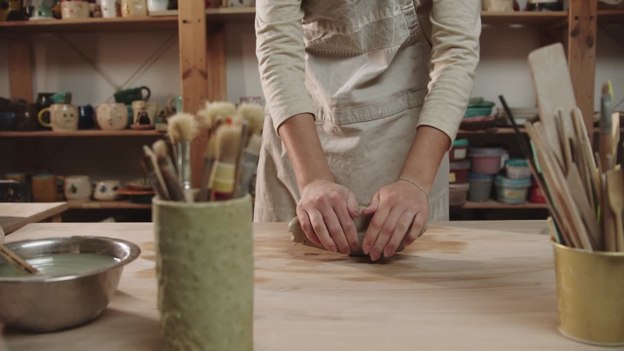 mujer alfarera amasa arcilla en la mesa en el estudio de arte - pinceles y otras herramientas de pie en primer plano