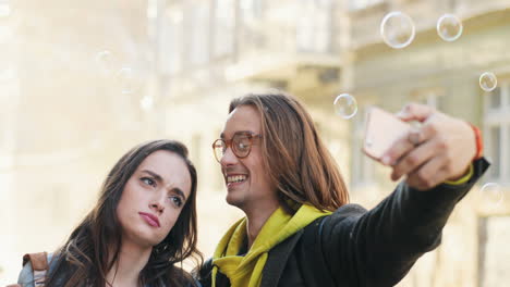 vista de cerca de una joven pareja caucásica de amigos tomándose selfies mientras caen bolas transparentes de jabón