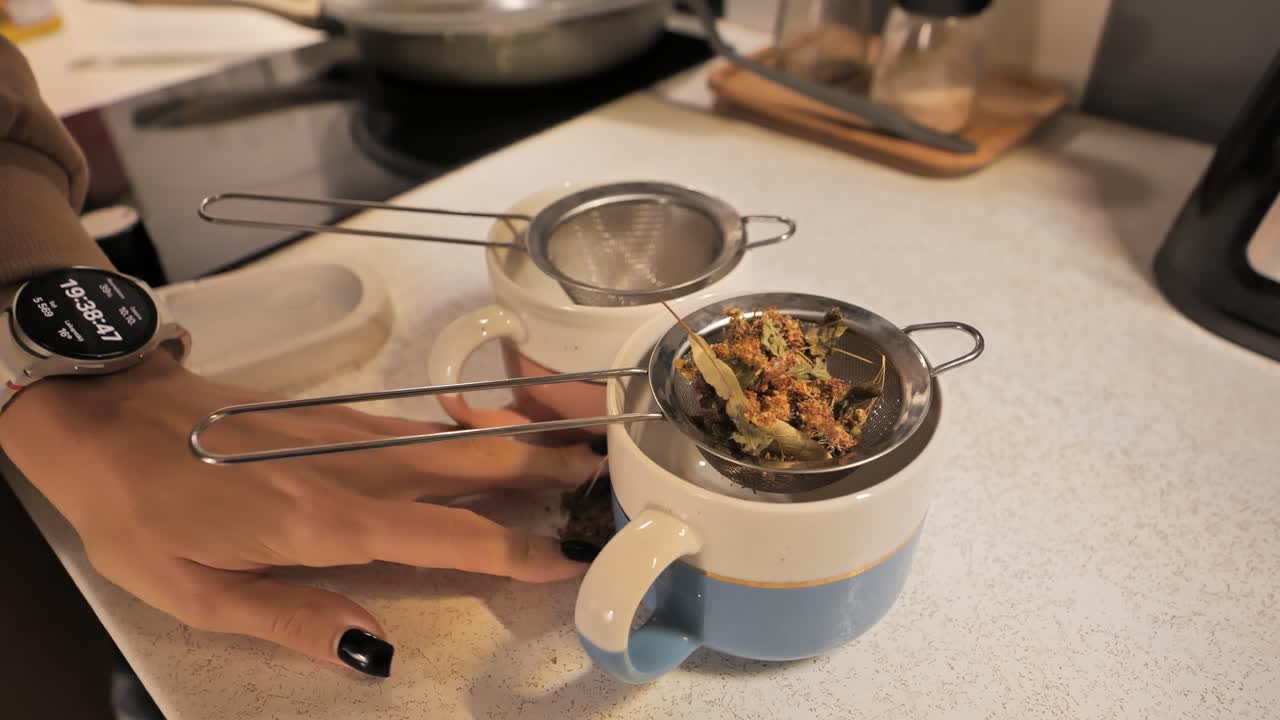 Herbal tea blend being added to strainers in cups for brewing - 4K.