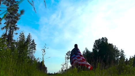 low angle footage of a man holding an american united states flag on his shoulders and walking into the distance on a rural countryside sunny summer road and begins to wave the flag in slow motion.