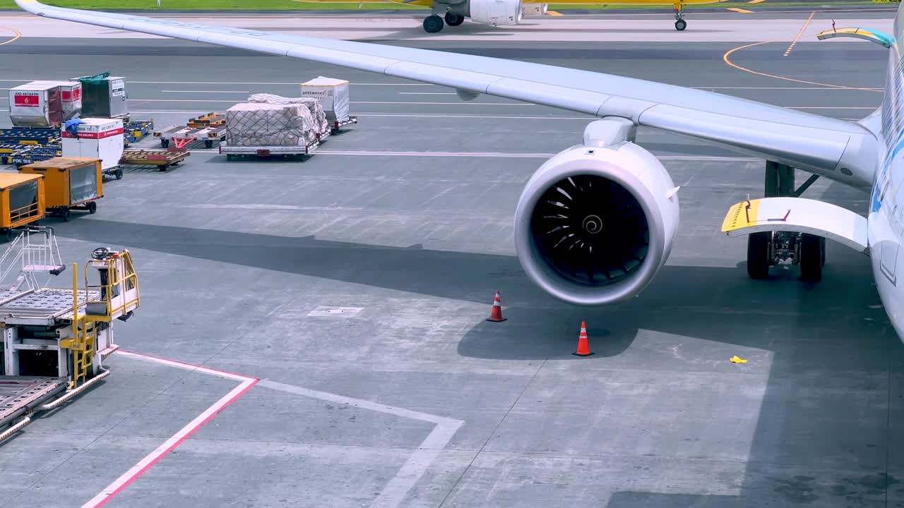 Detailed view of a modern jet engine and wing during airport ground operations, with cargo containers and equipment ready for loading