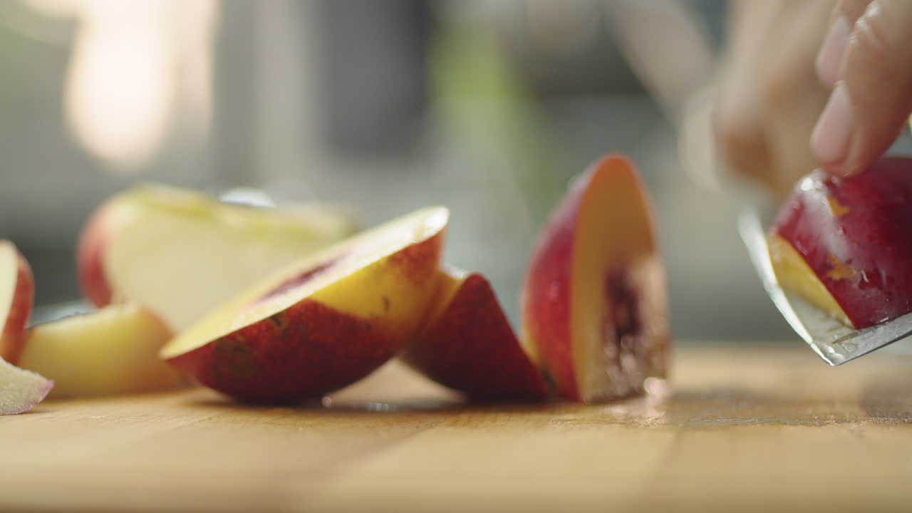 un joven cortando un melocotón sobre una mesa de madera en la cocina para preparar un batido de frutas.