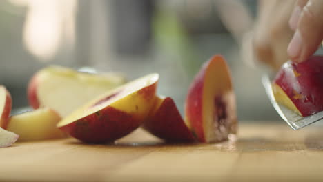 Young-guy-cutting-a-peach-on-wooden-table-in-kitchen-for-prepare-a-fruit-milkshake