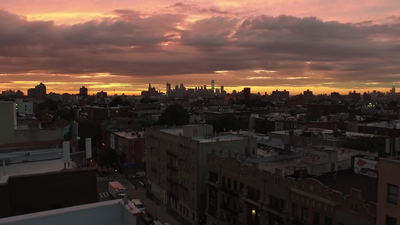Rising NYC sunset aerial view over Brooklyn rooftops revealing Manhattan skyline 4K