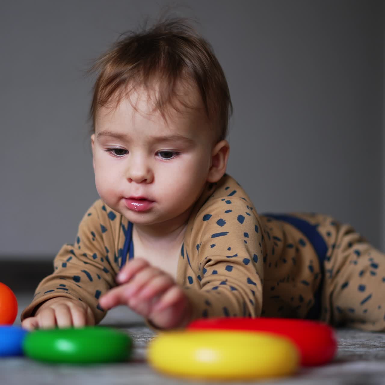 Cute Caucasian baby boy lies on the carpet in the room. Adorable child pulling his toys into his mouth. Blurred backdrop