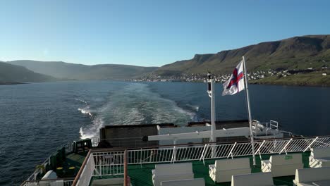 wide shot of waving flag on smyrill ferry and tvororyi island in background