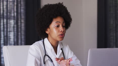 African-american-female-doctor-talking-on-videocall-on-laptop-while-sitting-at-home