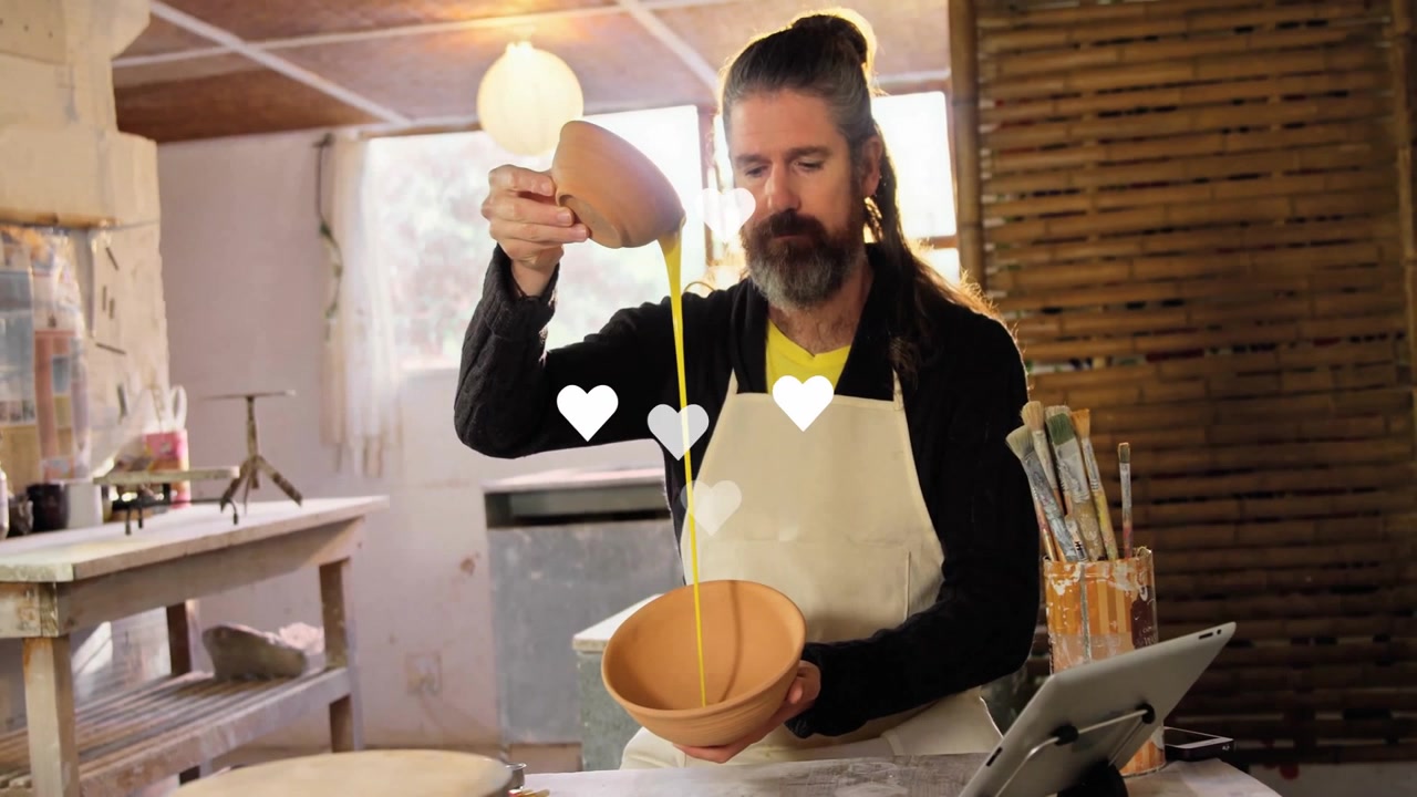 Vasaio che solleva una ciotola e versa engobbio giallo per la decorazione mentre icone a forma di cuore fluttuano e svaniscono.