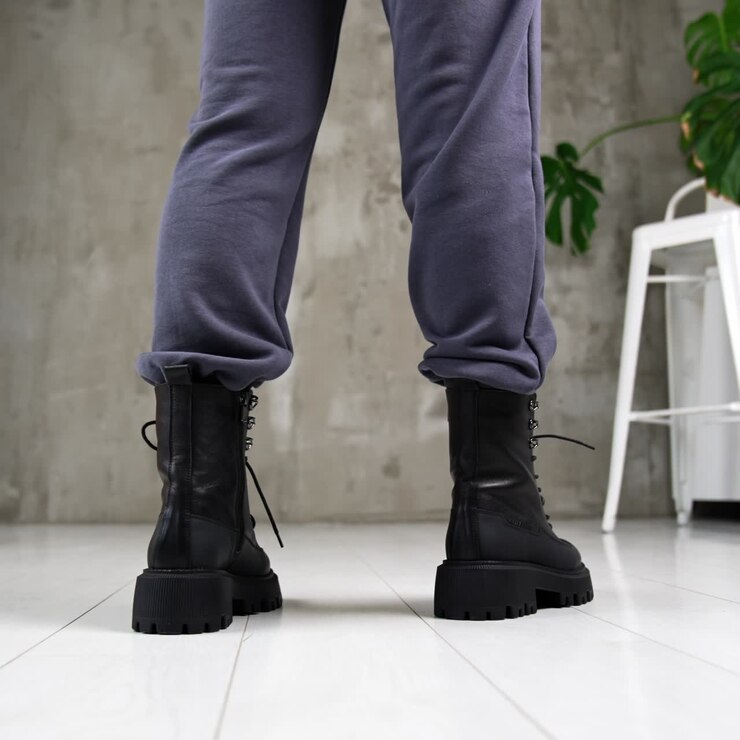 Female model standing her back to camera in black tractor boots. Woman demonstrating the modern stylish footwear in studio