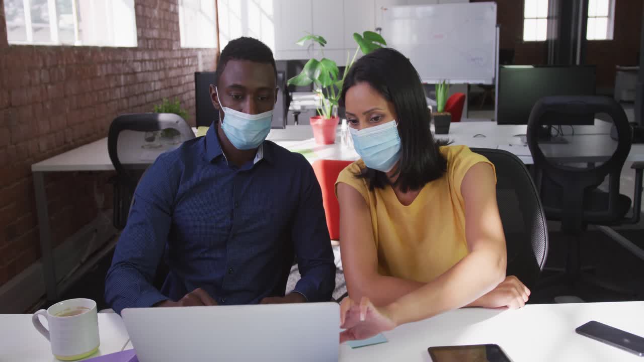 diversos colegas de negocios masculinos y femeninos con máscaras faciales sentados en el escritorio usando una computadora portátil