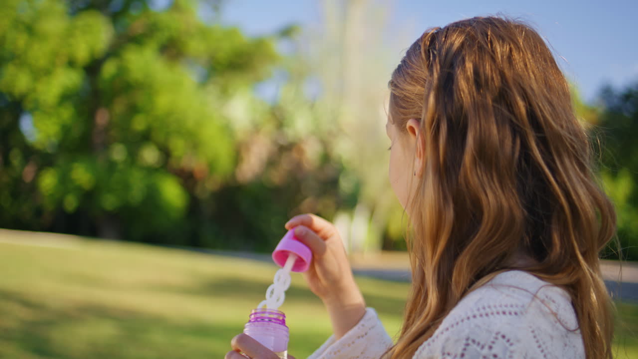 Girl blowing soap bubbles in sunny park portrait. Cute kid playing in nature