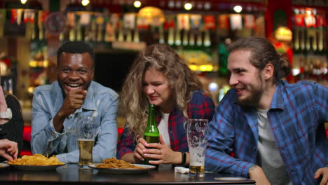 The-man-tells-a-joke-in-the-company-of-friends-sitting-at-the-table.-Girls-and-men-laughing-while-sitting-at-a-bar-at-a-table-with-beer.