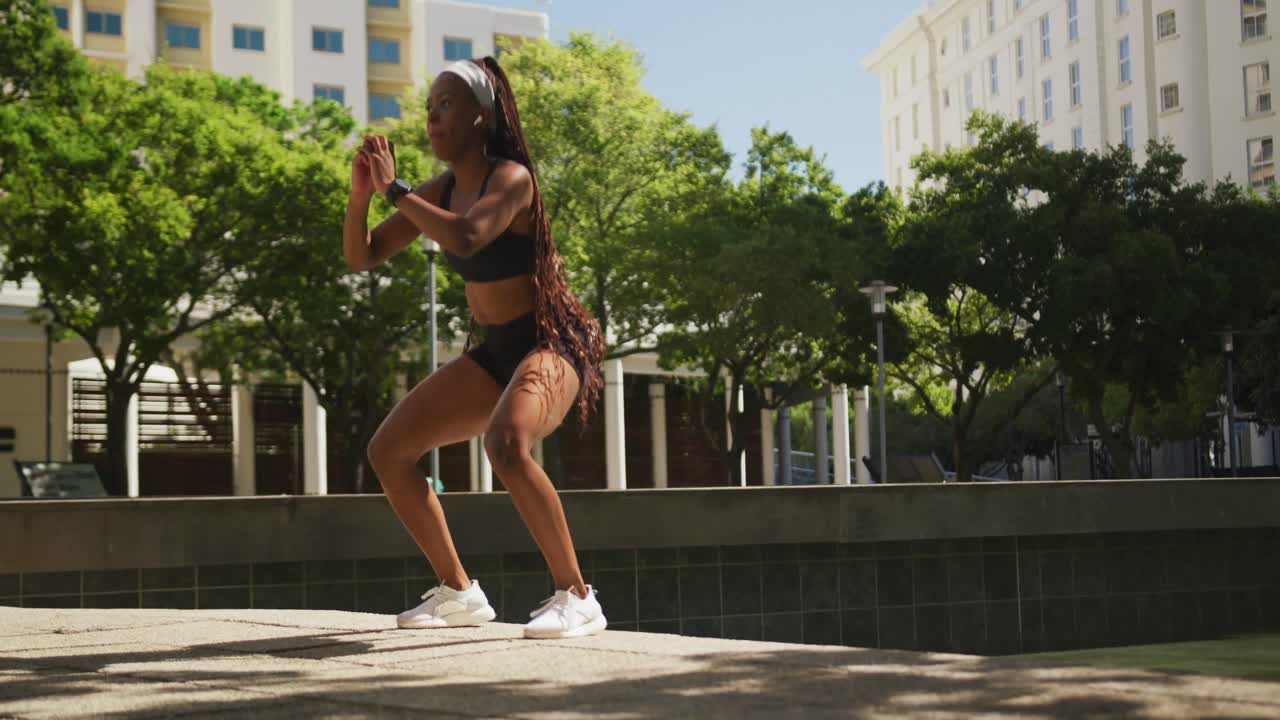 mujer afroamericana con auriculares inalámbricos haciendo ejercicio al aire libre saltando escaleras en la ciudad