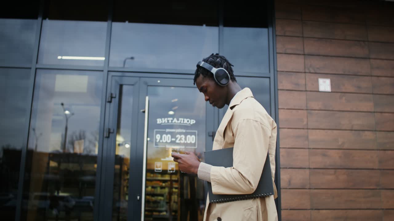Man using phone and wearing headphones outside building