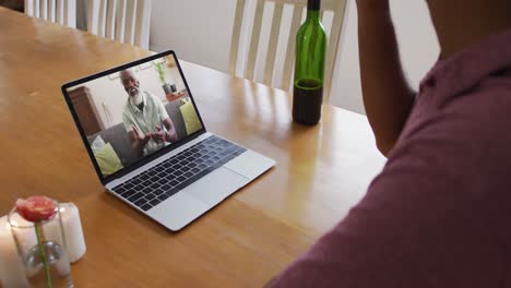 Mid-section-of-african-american-man-drinking-wine-while-having-a-video-call-on-laptop-at-home