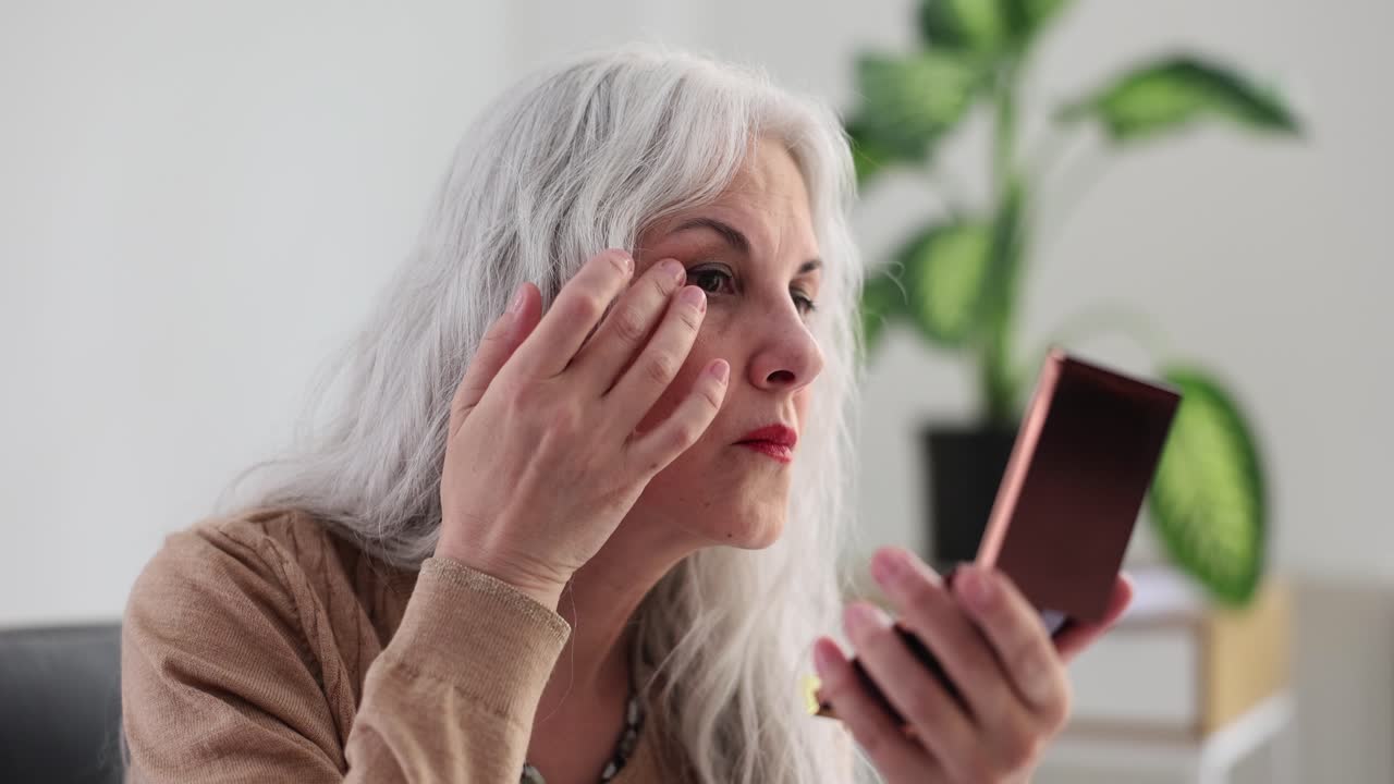 Elderly woman applying makeup looking in a small mirror