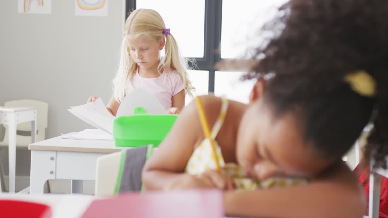 Video of focused diverse girls sitting at school desks and learning