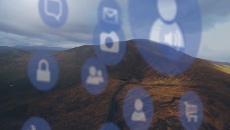 digital interface icons floating over winding road cutting through brown hills under cloudy sky