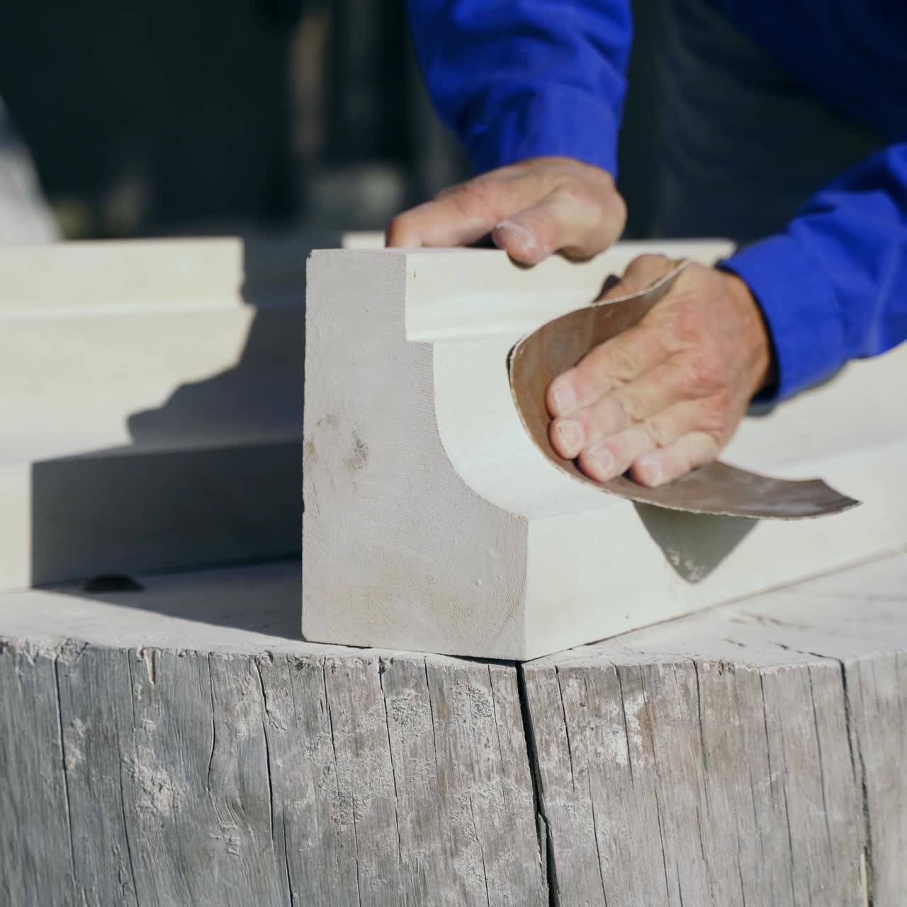 master is polishing a wooden product with an emery cloth by his hands on a stump in the street in the afternoon.