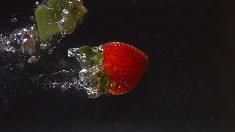 a strawberry and piece of kiwi are dropped into water and sink