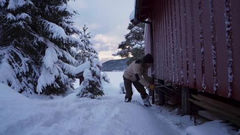 Man-Is-Walking-Towards-Under-The-Cottage-To-Get-The-Snow-Pusher