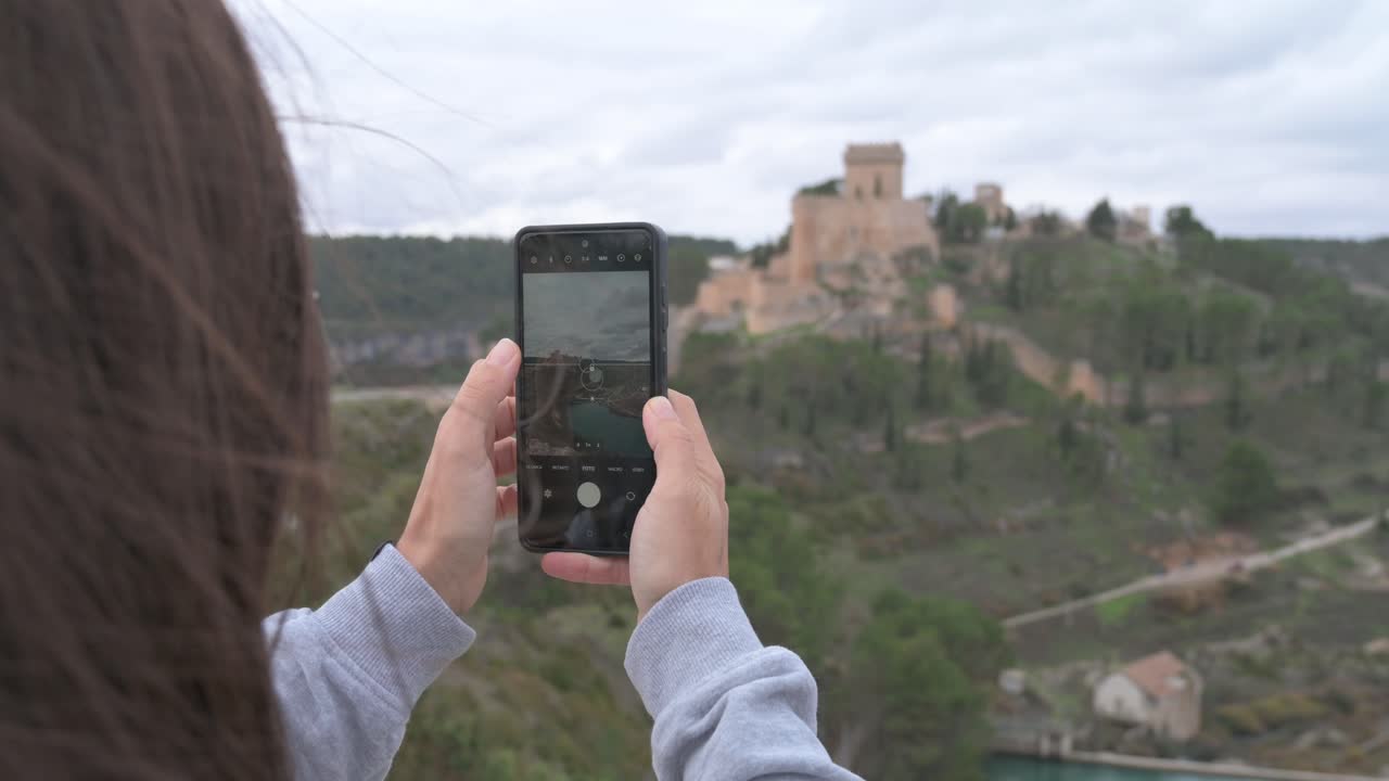 Joven turista fotografiando la ciudad de Alarcón con su teléfono móvil.