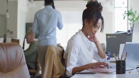 mulher de negócios afro-americana feliz usando laptop com colegas no escritório criativo