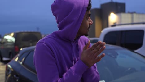 young sri lankan man trying to warm hands while standing in parking lot