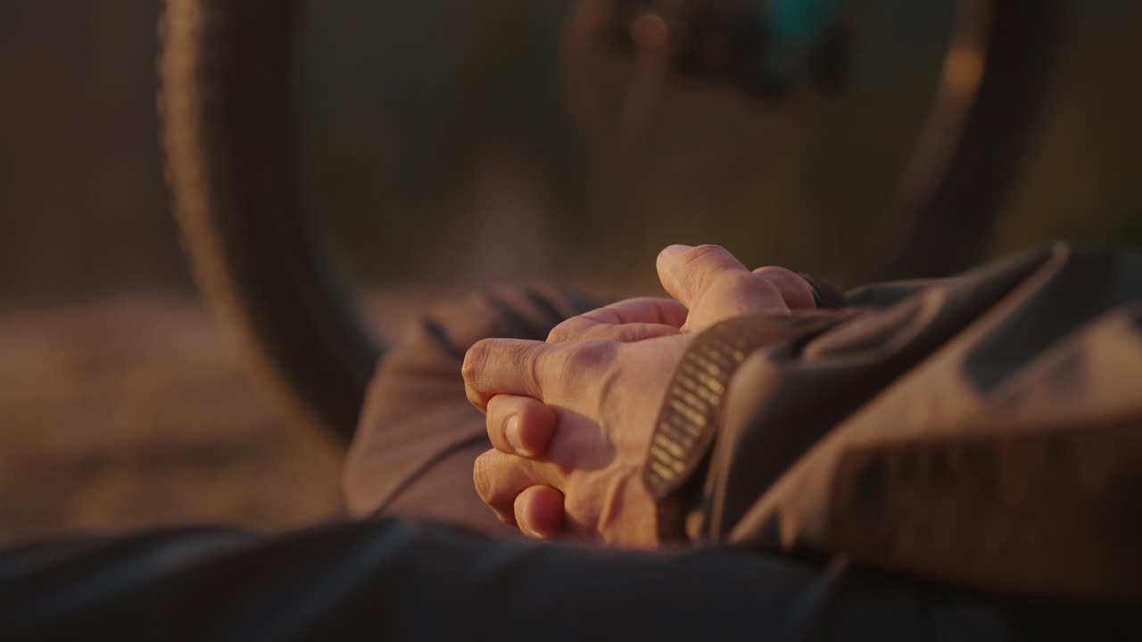 Man rests with hands clasped in front of bike during a warm sunset outdoors