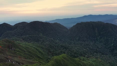 Aerial-pedestal-up-shot-of-sunrise-behind-green-mountains-around-Mount-Sibayak-and-Mount-Sinabung-in-North-Sumatra,-Indonesia