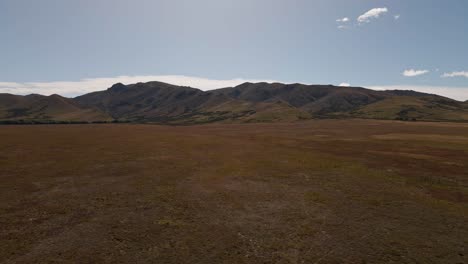 Wavy-mountain-range-behind-flat,-dry-plains-within-sunny-prairie-landscape