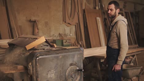 the master in overalls inserts a large rail into the grinding machine, pulls it out. joiner's workshop