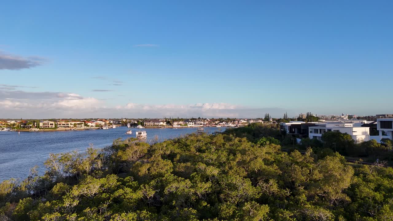 Riprese con drone catturano un sereno paesaggio costiero con tenute di lusso e barche durante il tramonto, evidenziando una vegetazione lussureggiante e acque calme.