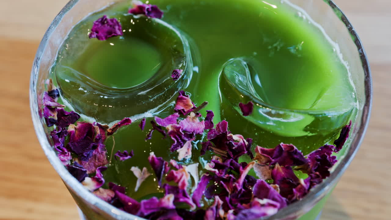 Primer plano de un té matcha con hielo en un vaso con flores moradas secas encima