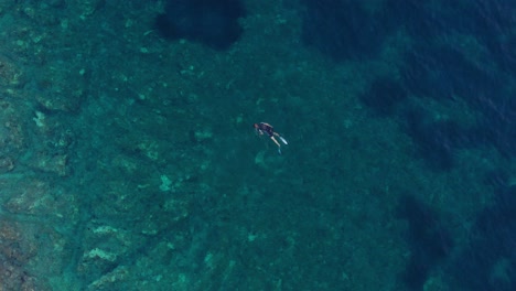 Hombre-Buceando-En-Círculos,-Agua-Cristalina,-Vista-Aérea-De-La-Playa-Rocosa