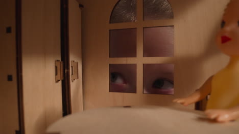 Interested-girl-peeks-into-window-of-dollhouse-in-dark-room