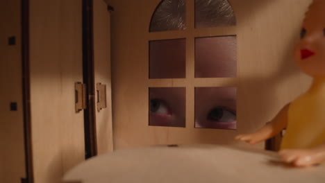 interested girl peeks into window of dollhouse in dark room