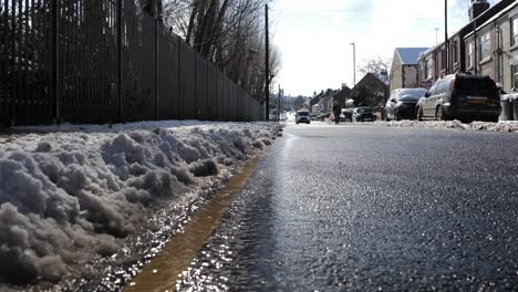 a stream of water by the side of a road as snow and slush melts in the sun