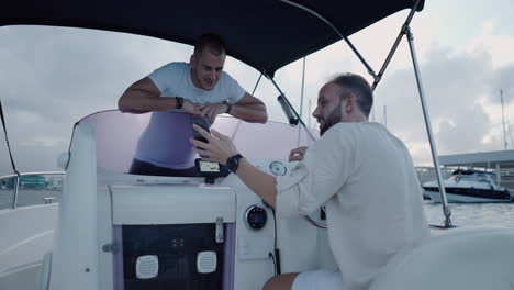 two men on a boat interacting with a smartphone at a marina