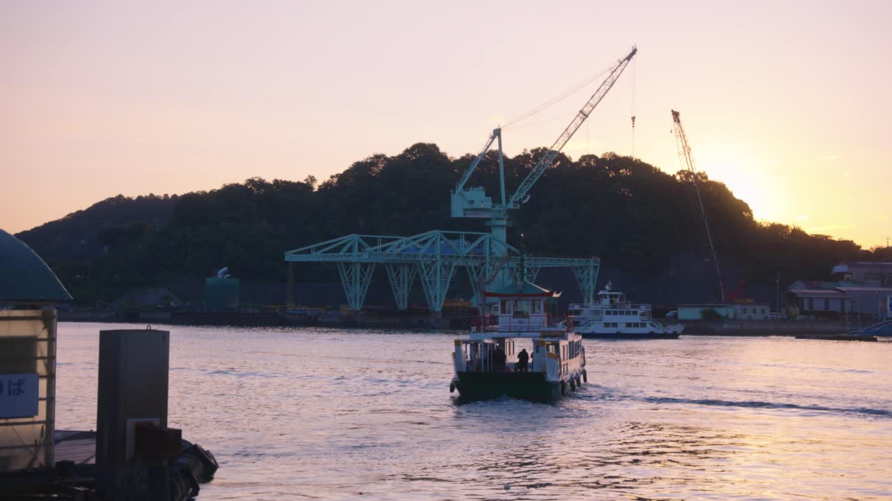Sunset over a Japanese port with a ferry and construction cranes