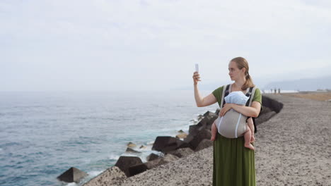 A mother and her baby make the most of a sunny summer day by the sea. The child is carried in a kangaroo backpack as they revel in nature&#039;s splendor