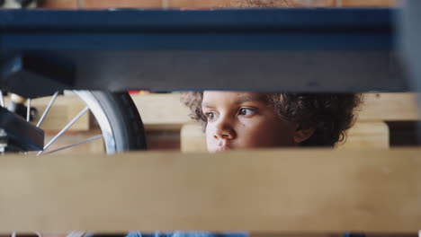 close up of pre teen mixed race boy inspecting his racing kart in the garage, seen through kart frame, selective focus